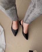 Μαύρες μυτερές εξώφτερνες slingback γόβες από συνθετικό δέρμα φορεμένα σε γυναικεία πόδια με γκρι στενό παντελόνι πλάνο από ψηλά