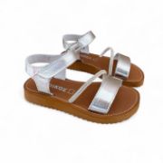 Δερμάτινα παιδικά πέδιλα για κορίτσια σε ασημί χρώμα με αυτοκόλλητο κούμπωμα και στρας και καφέ σόλα πλάγια όψη σε λευκό φόντο.