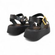 Γυναικεία σανδάλια δίσολα flatform με μαύρη σόλα και μαύρη μπαρέτα με χρυσή αγκράφα και λοξό λουρί στο κουντεπιέ με χρυσά τρουκς και μαύρη φάσα στα δάχτυλα πίσω όψη σε λευκό φόντο.