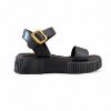 Γυναικεία δερμάτινα δίσολα σανδάλια flatforms με μαύρη σόλα, μαύρη μπαρετα με χρυσή αγκράφα και μαύρη φάσα στα δάχτυλα πλάγια εξωτερική όψη σε λευκό φόντο.