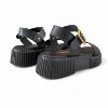 Γυναικεία δερμάτινα δίσολα σανδάλια flatforms με μαύρη σόλα, μαύρη μπαρετα με χρυσή αγκράφα και μαύρη φάσα στα δάχτυλα πίσω όψη σε λευκό φόντο.