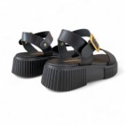 Γυναικεία δερμάτινα δίσολα σανδάλια flatforms με μαύρη σόλα, μαύρη μπαρετα με χρυσή αγκράφα και μαύρη φάσα στα δάχτυλα πίσω όψη σε λευκό φόντο.