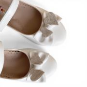 Παιδικές μπαλαρίνες σε λευκό χρώμα με μπαρέτα με αυτοκόλλητο κοπύμπωμα στο κουντεπιέ και δικαοσμητικό λευκό φιογκάκι με καρδιέσ από στρας.Κοντινό στο φιογκάκι σε λευκό φόντο.