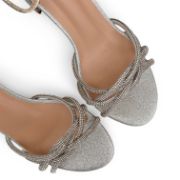 Γυναικεία πέδιλα από γκλίτερ σε ασημί χρώμα με λουράκια από στρας στα δάκτυλα σε πλεκτό σχήμα κοντινό στα λουράκια σε λευκό φόντο.